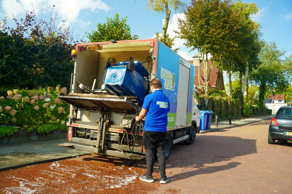 Een container wordt achter op de Frisse Kliko-wagen in de wasinstallatie geschoven.